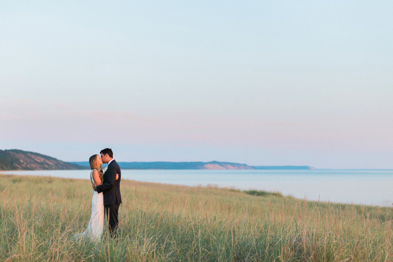 Romantic bride & groom kissing at sunset in the dune grass along Lake Michigan in Elberta, Michigan