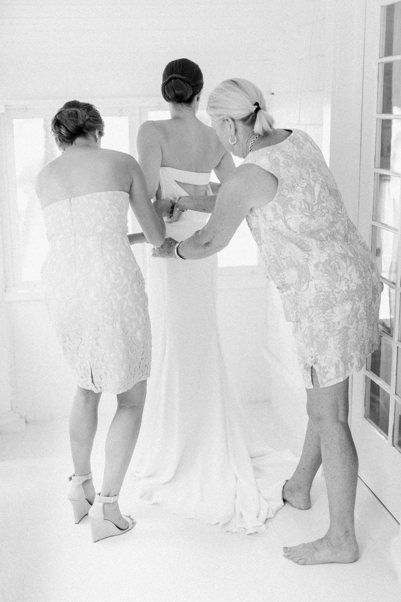 Bride putting on her wedding dress with family
