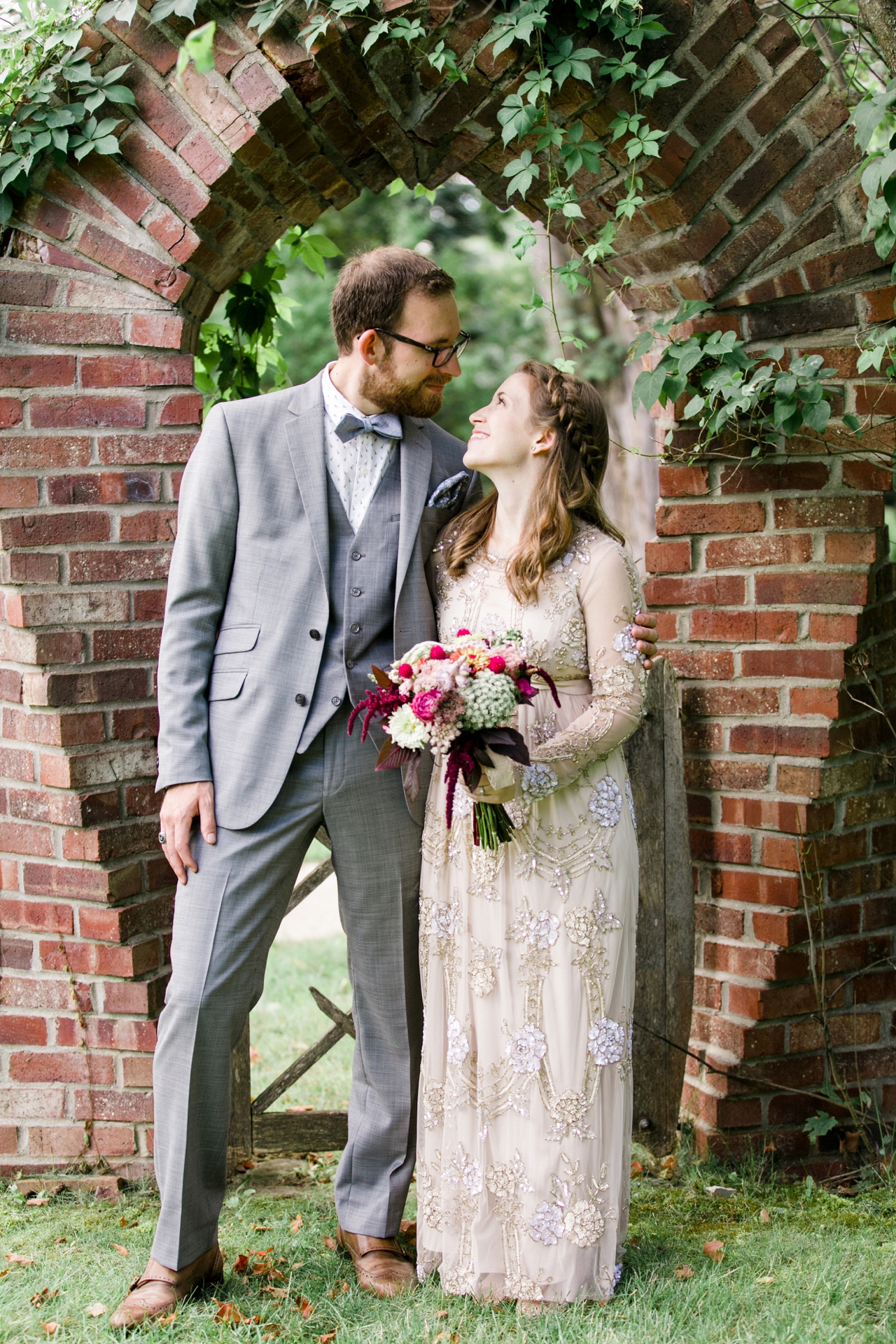This is a photo of a bride and groom in front of a brick arch covered in vines. 