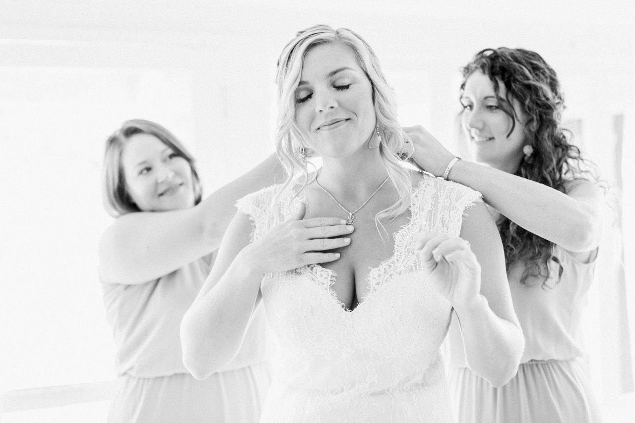 This is a bride touching a necklace that was her mothers and closing her eyes while her bridesmaids help her put in on