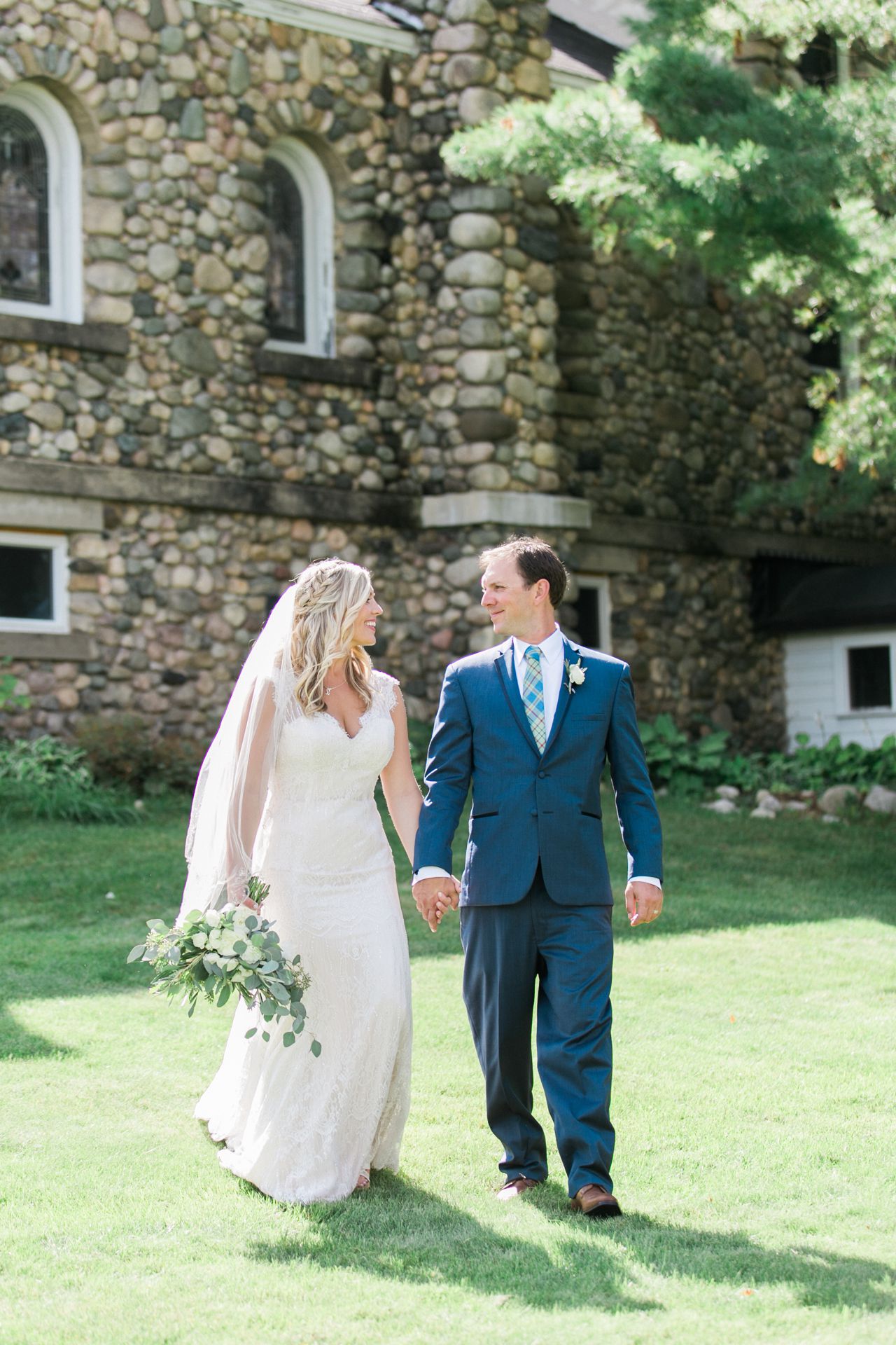 This is a bride and groom outside a church in Lake Leelanau walking and smiling while holding hands