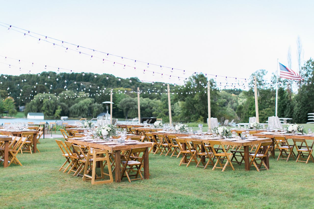 This is a photo of a wedding reception with wooden table and chairs under string lights