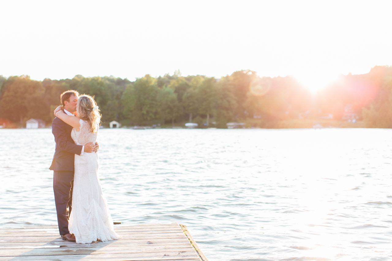 This is a photo of a bride and groom kissing on a dock with Lake Leelanau in the background as the sun sets