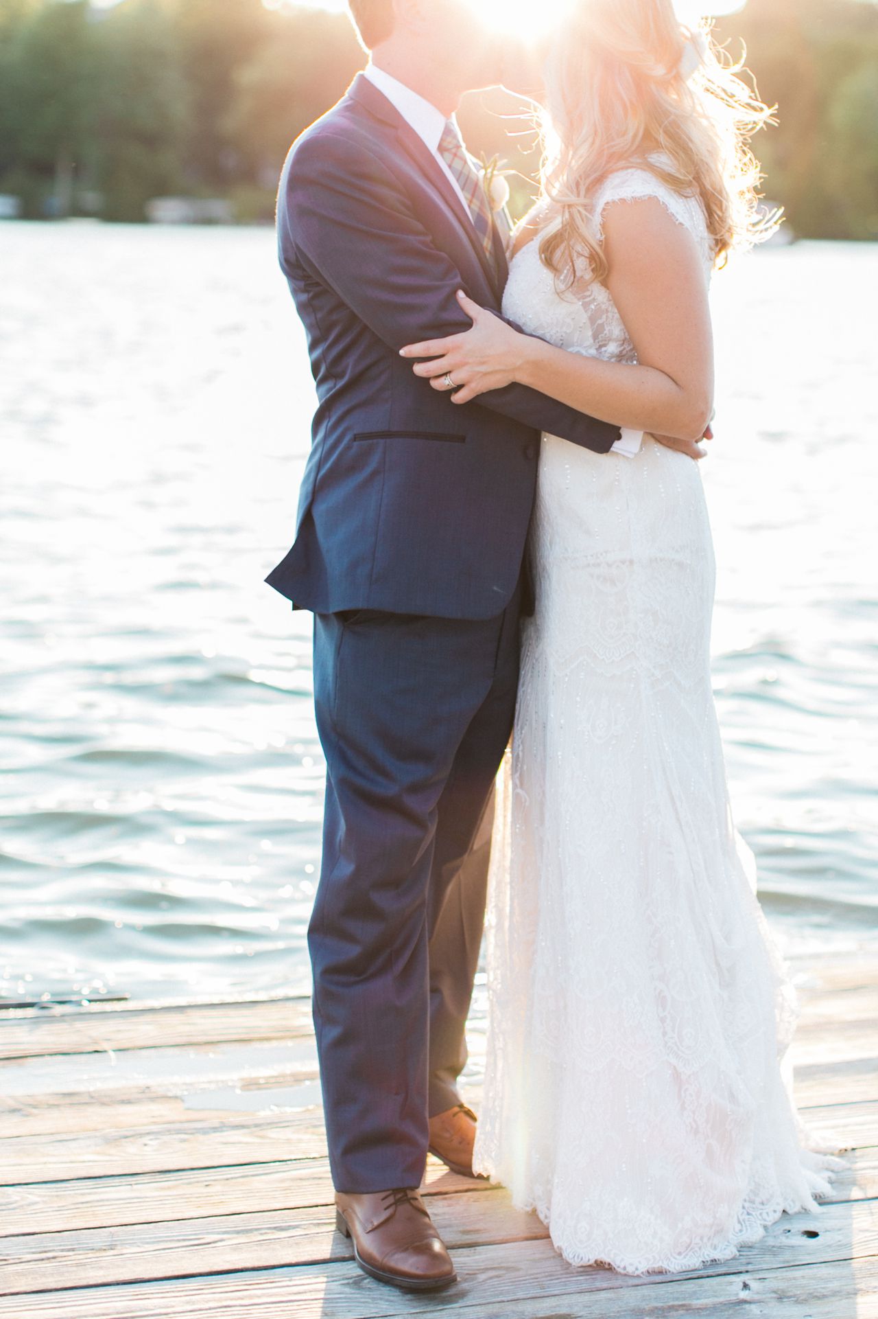 This is a bride and groom kissing on a dock with Lake Leelanau in the background as the sun sets