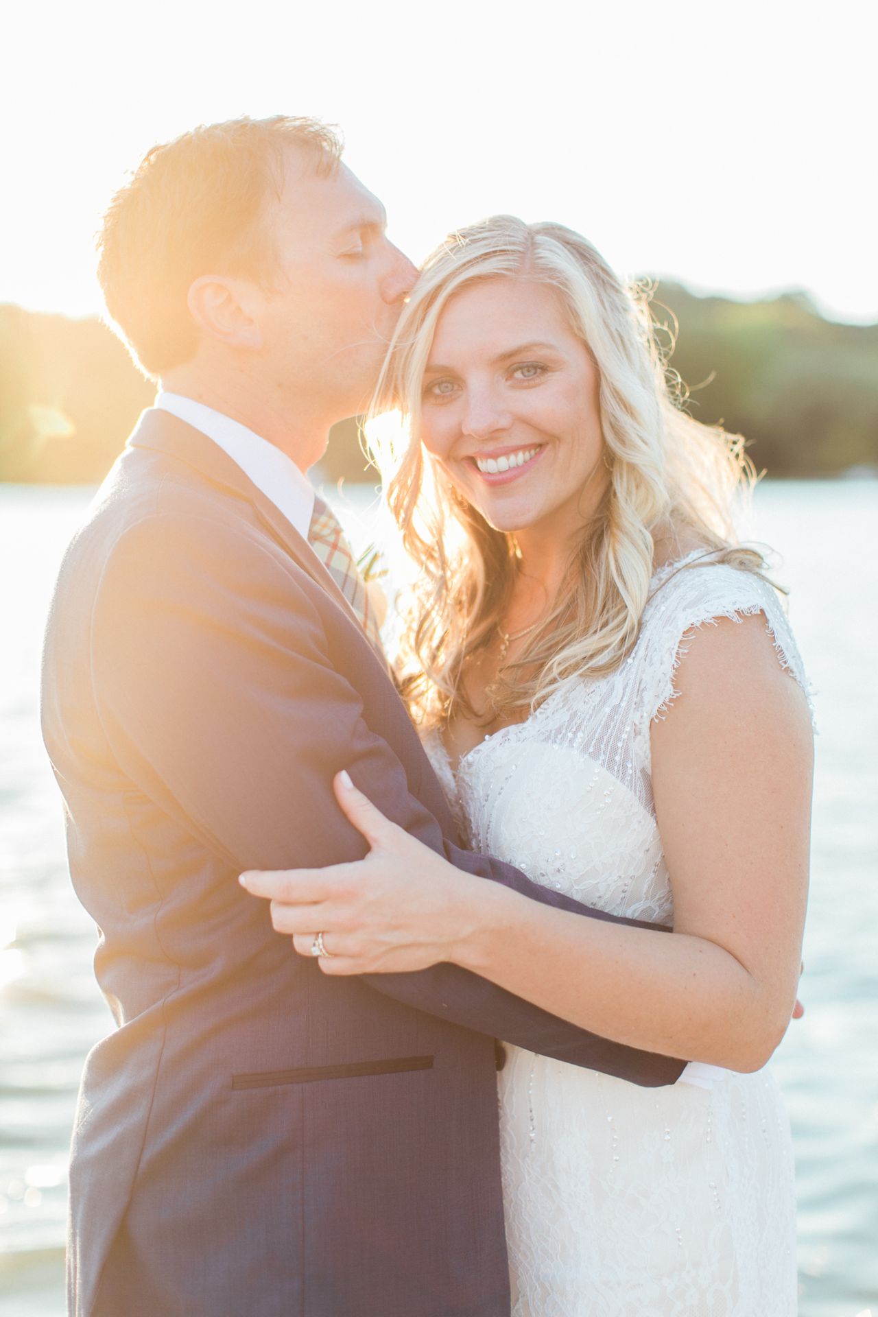 This is a photo of a groom kissing the brides temple with Lake Leelanau in the background as the sun sets