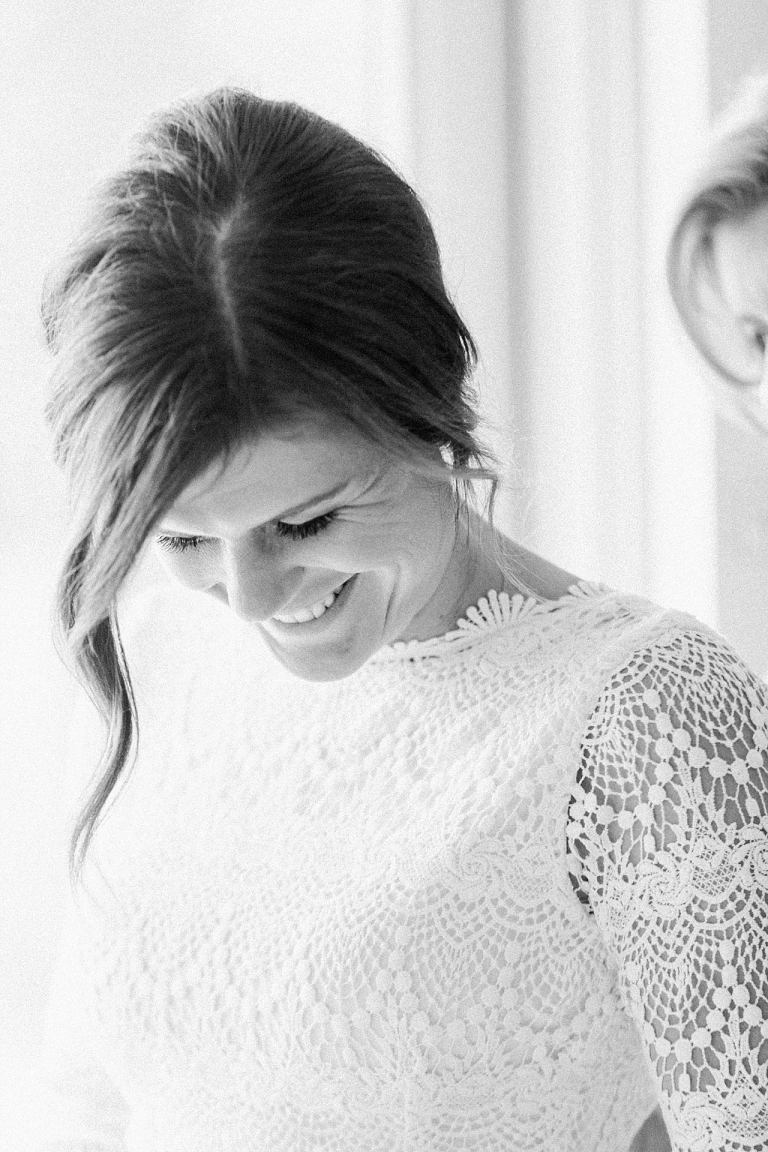 A bride smiling while putting on her lace wedding dress