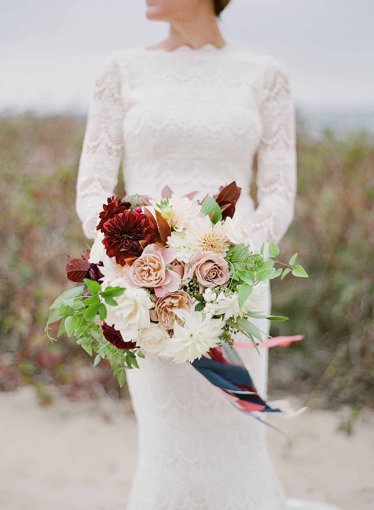 A bridal bouquet with pink, white, and burgundy flowers with navy blue ribbon 