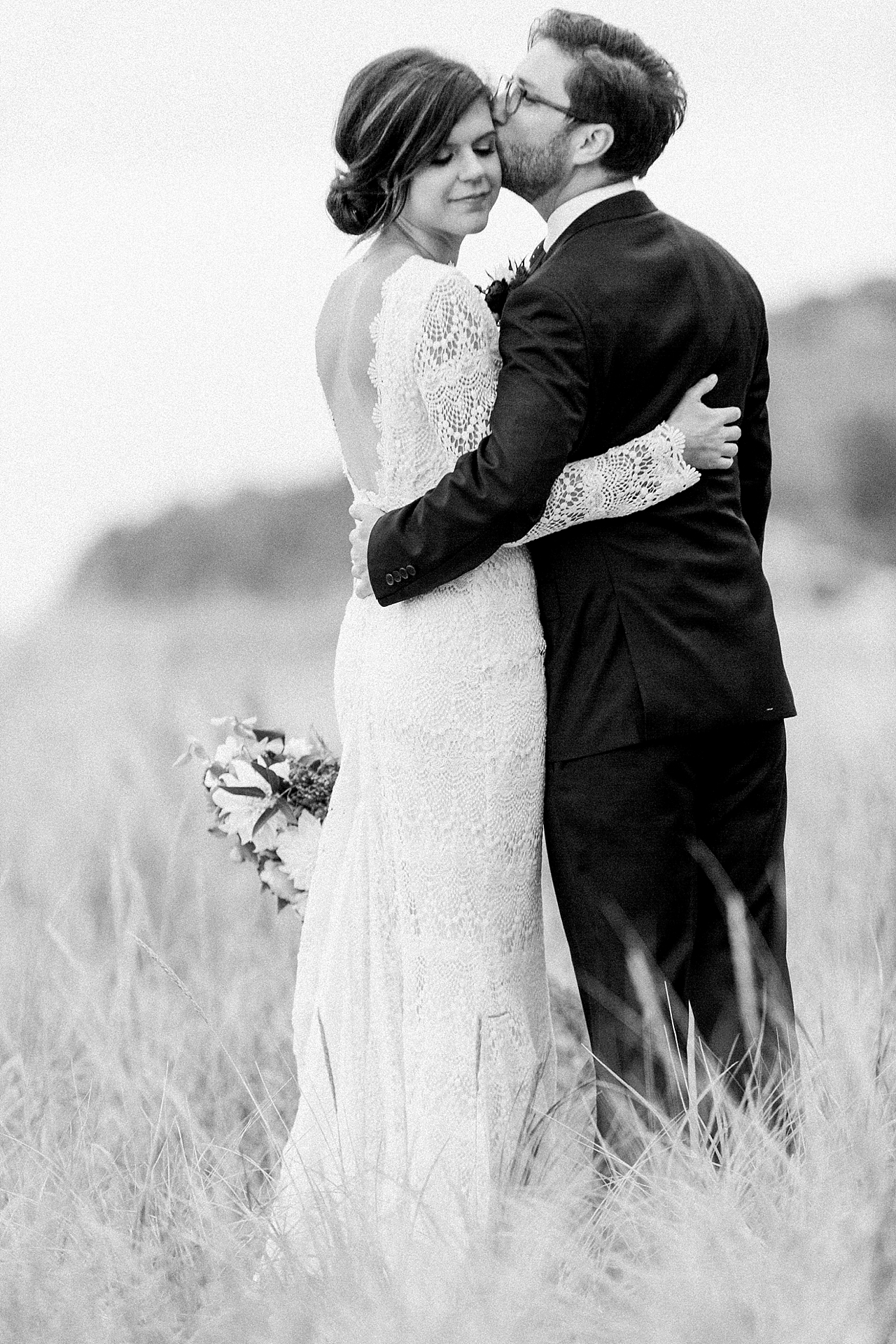 A groom kissing a brides cheek in sand dunes along the water in Northern Michigan