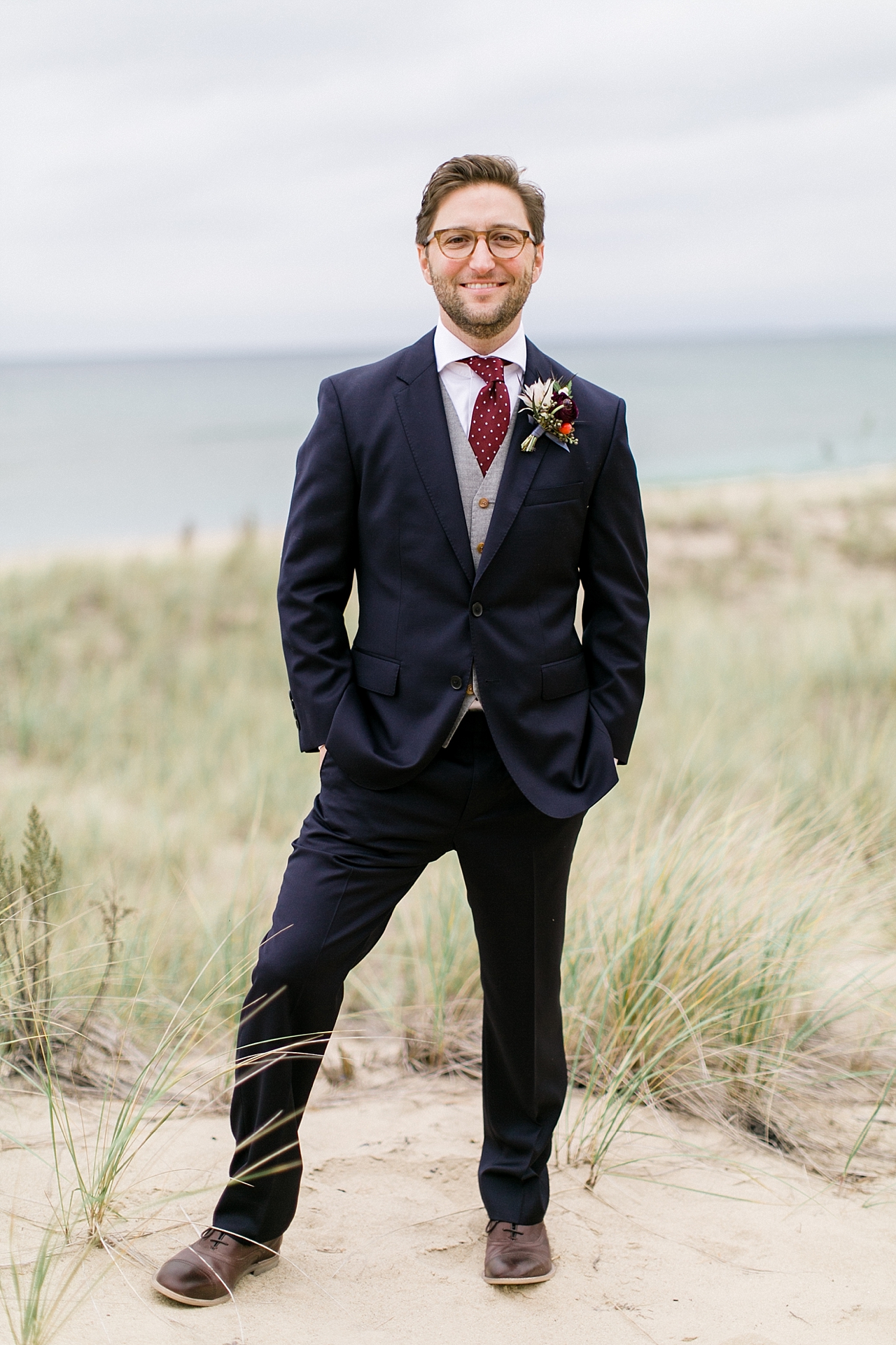 A groom standing in sand dunes by Lake Michigan
