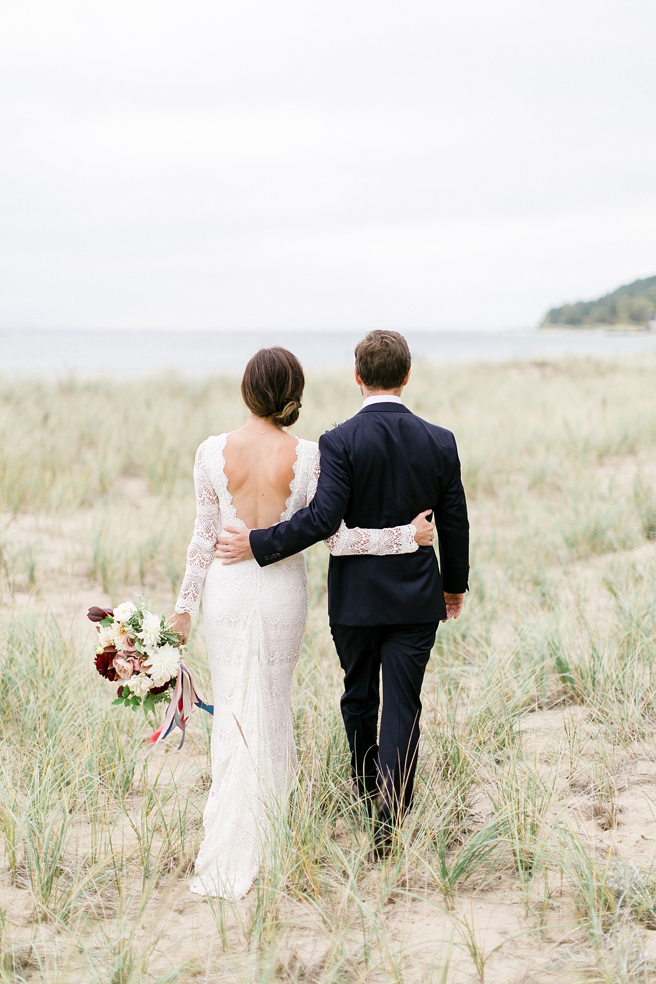 A bride and groom walking through sand dunes in the fall along Lake Michigan