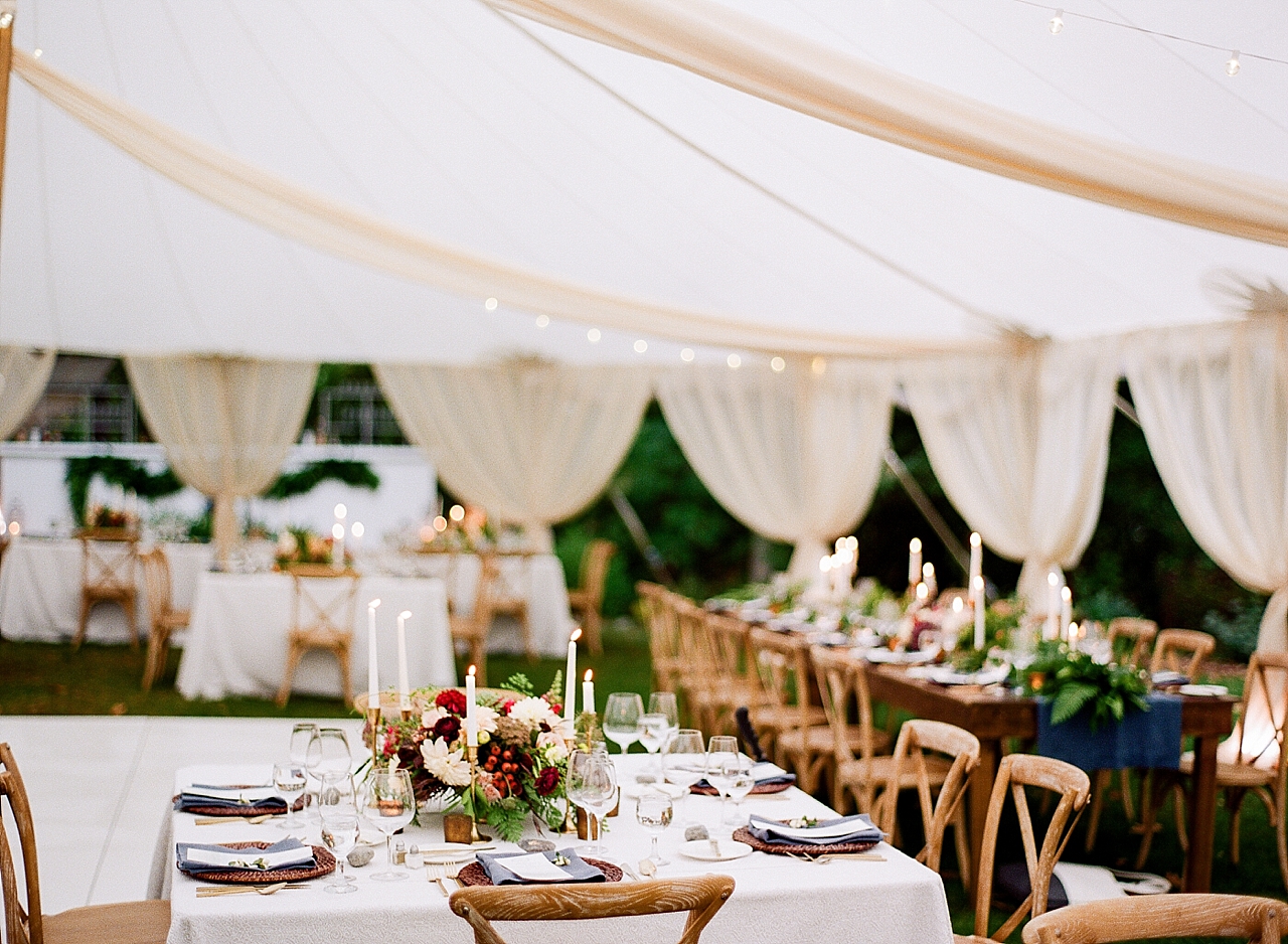 The reception tent with wooden chairs, greenery, and burgundy flowers at The Leelanau School