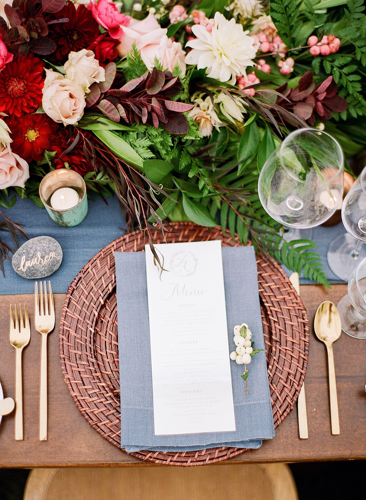 A table setting with a brown charger, blue napkin, white menu, and gold silverware at The Leelanau School