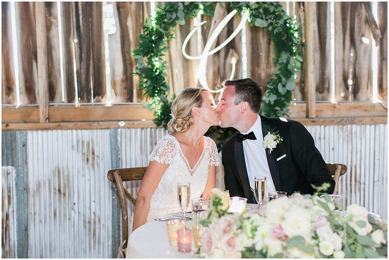 Bride and groom kissing at the sweetheart table inside of Shanahan's barn in Charlevoix, Michigan