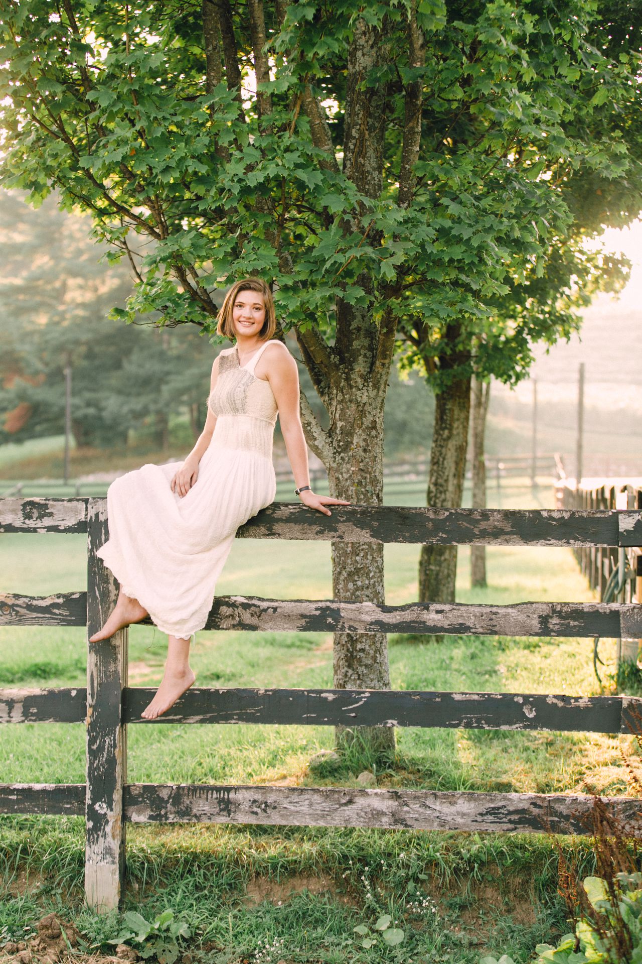 Young woman sitting on the fence of her horse pasture