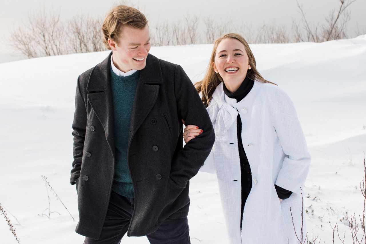 This is an engaged couple walking and laughing through snowy dunes in along the lake