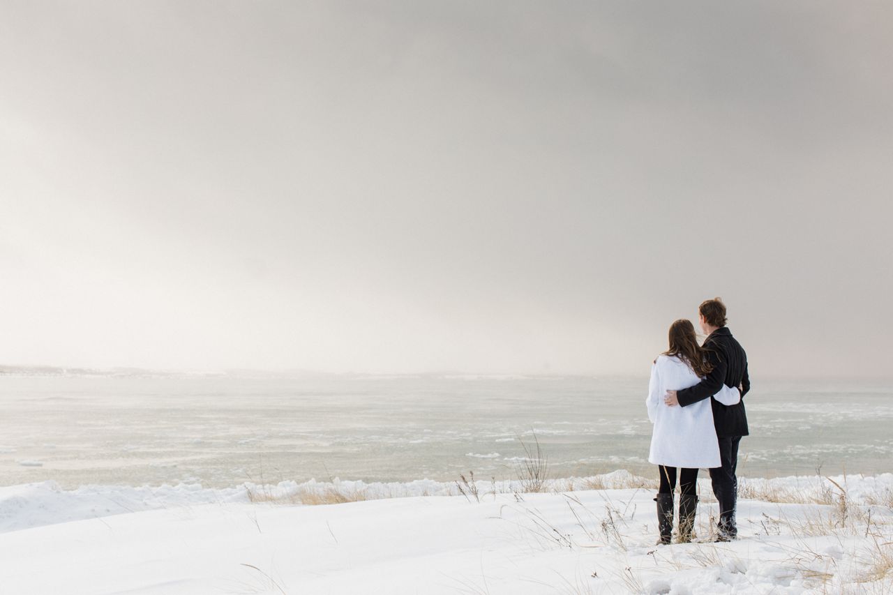 This is an engaged couple looking out at the lake as snow comes in