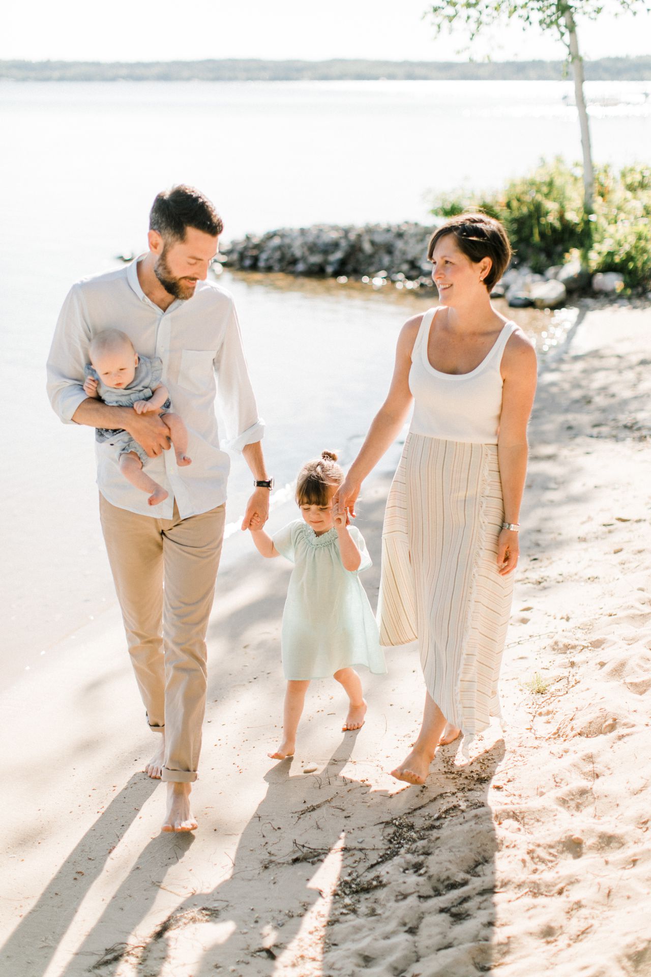 A family of 4 holding hands and walking along Crystal Lake in Northern Michigan