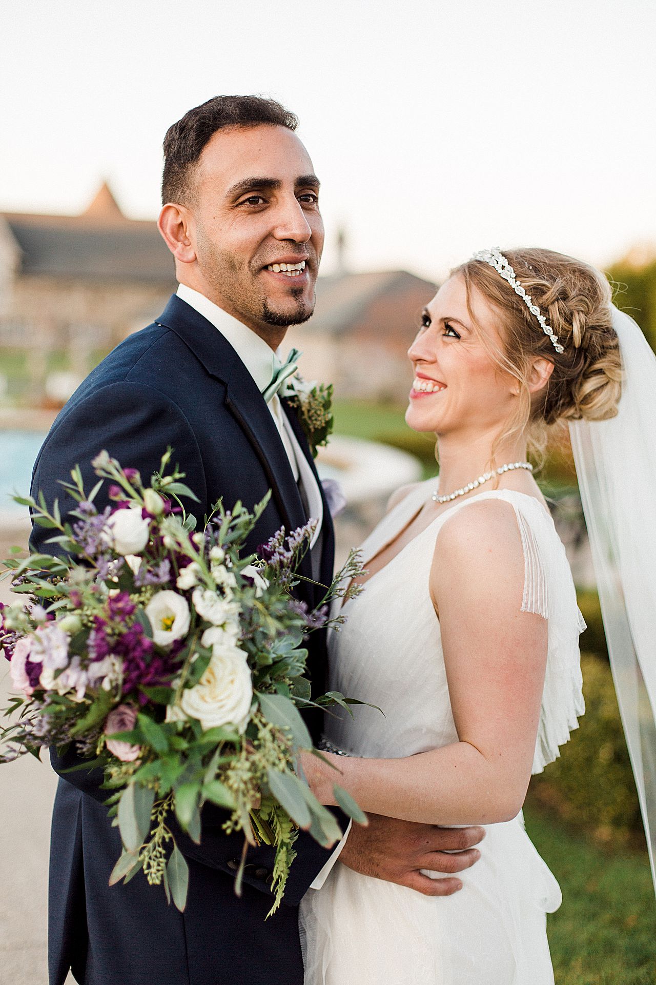 Bride and groom smiling while taking portraits in the Kings Grand Courtyard at Castle Farms in Charlevoix, Michigan with a fountain in the background