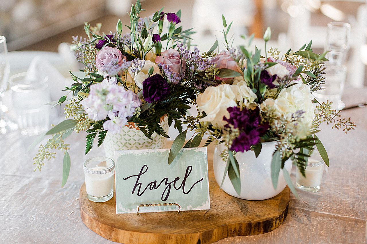 Purple flowers, green table card on a wooden slab on a reception table at Castle Farms