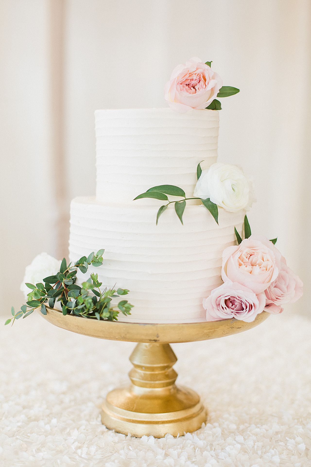 A 2 tier wedding cake with white frosting and peonies