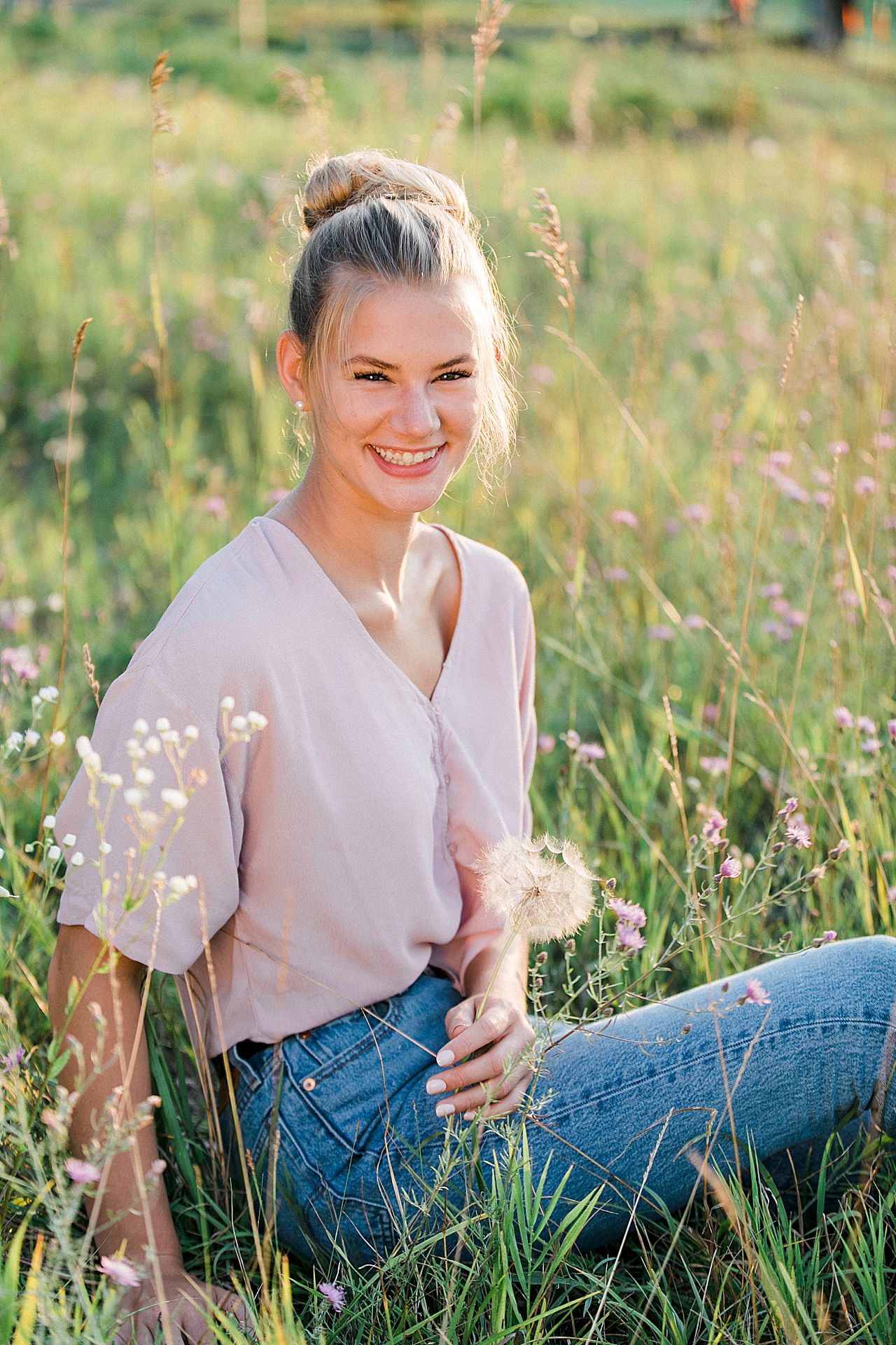 This is a senior portrait of a girl smiling in a field Boyne City, Michigan surrounded by pink flowers