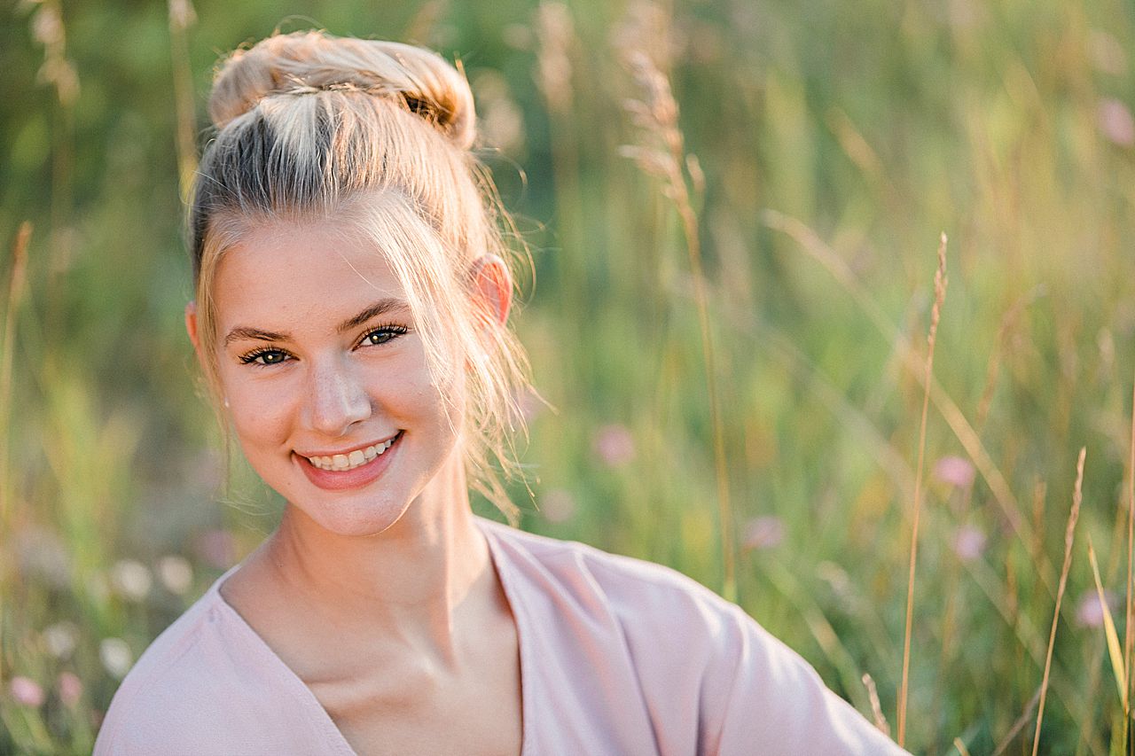 This is a high school senior at golden hour smiling at the camera near a lake in Northern Michigan