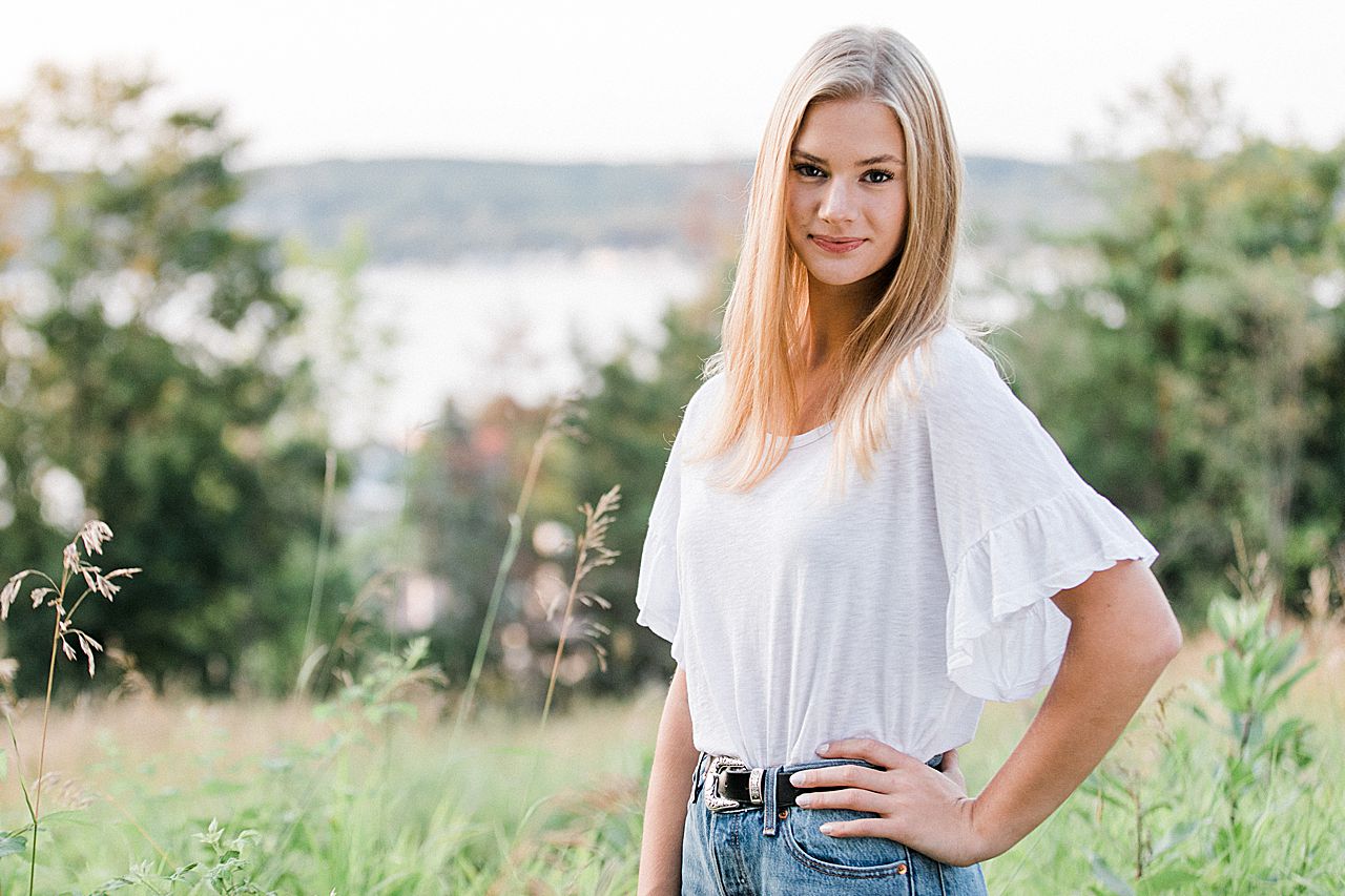 This is a senior portrait of a girl with her hand on her hip with the lake in the background in Northern Michigan