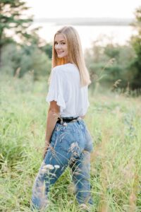 This is a senior portrait of a girl looking over her shoulder at the camera with a white shirt and blue jeans on