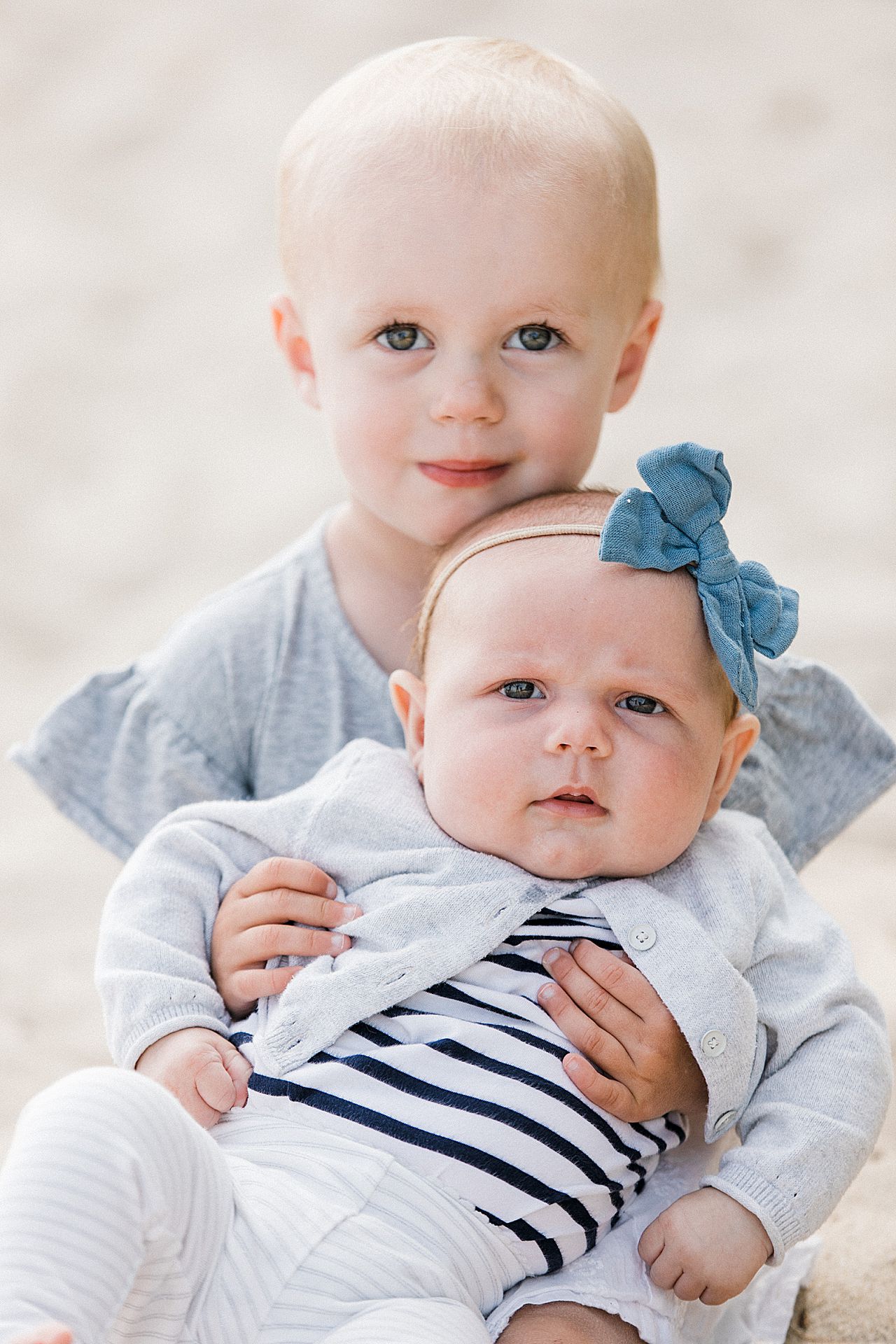 Older sister holding her baby sister on a beach in Michigan