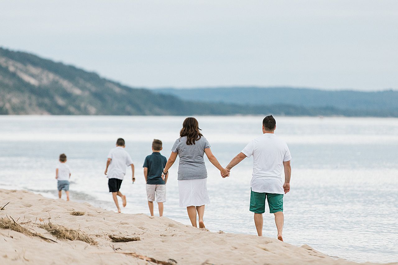 Couple holding hands and walking on the beach with their three sons