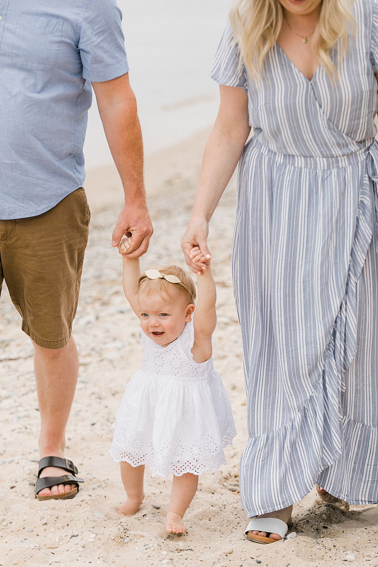 Mother and father holding their daughter's hand and walking on a beach