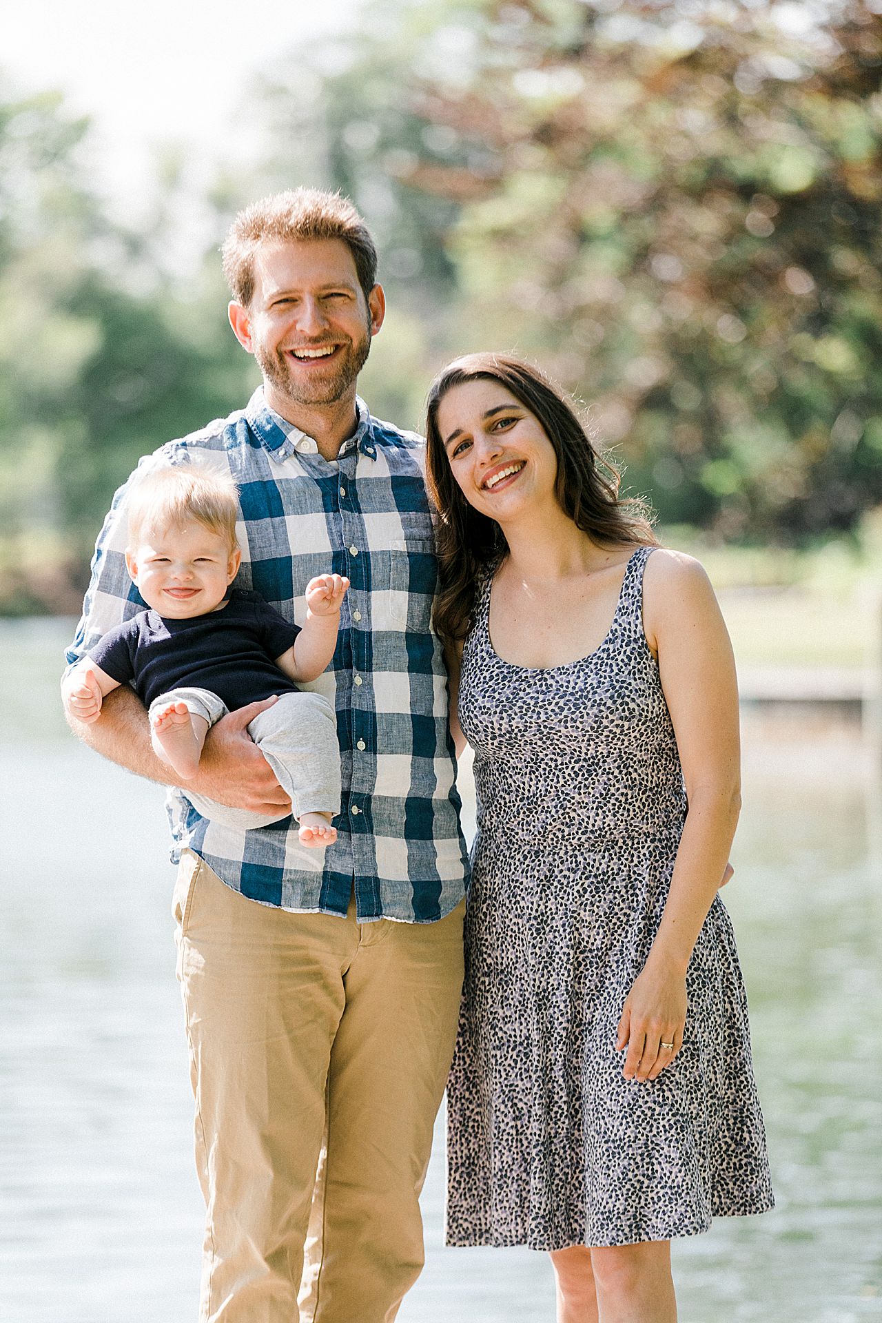 Mother and father smiling with their son in front of a lake