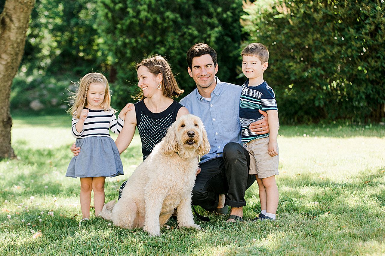 Family of four kneeling in the grass with their dog