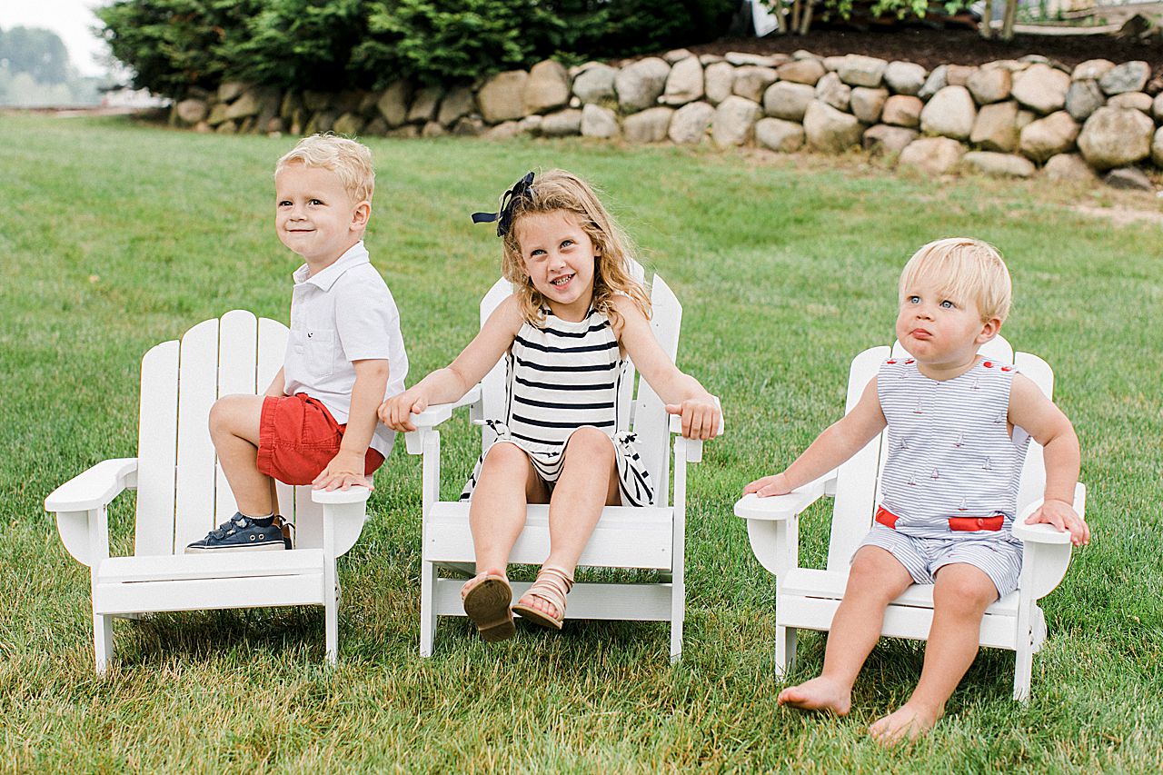 Three young cousins sitting in white lawn chairs in Northern Michigan