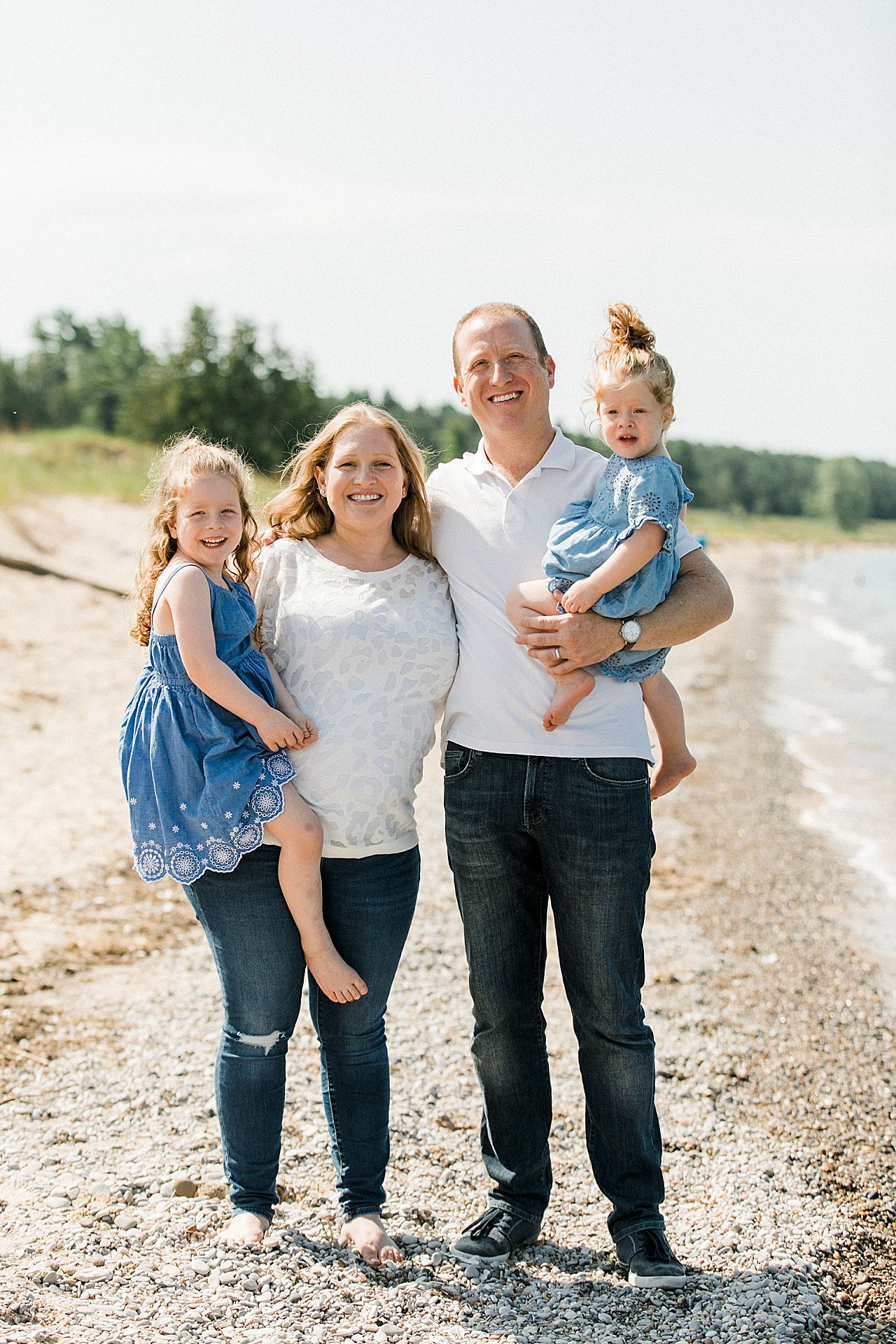 Parents holding their two young girls on a beach in Michigan