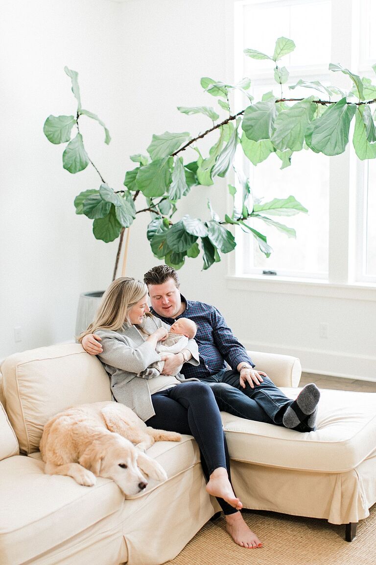 New parents sitting on their couch with their baby and golden retriever