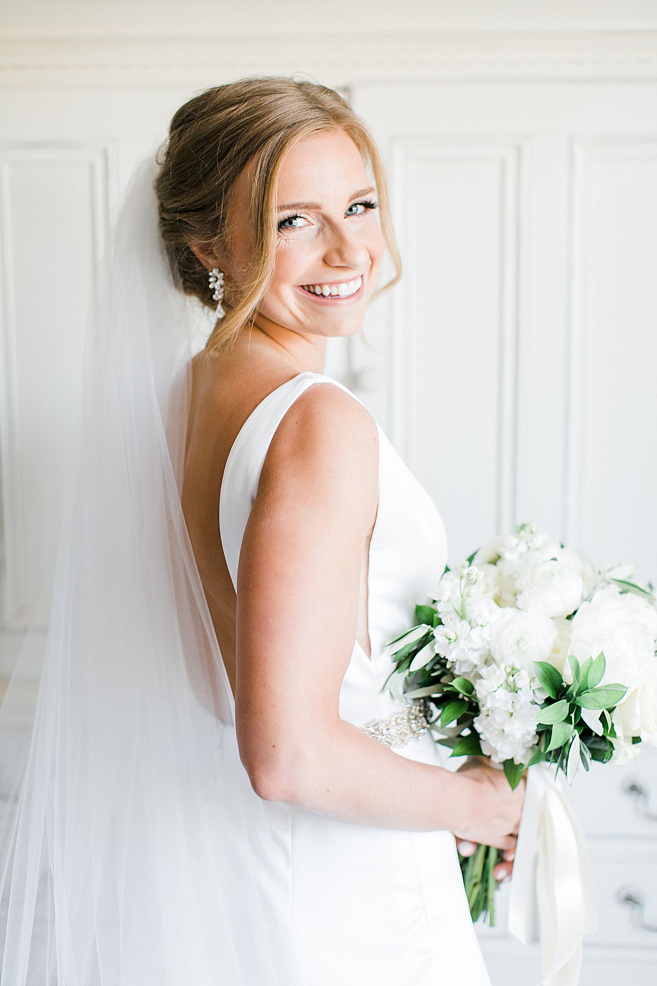 Bride looking back at the camera and smiling while holding her bouquet with white flowers