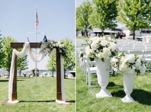 White ceremony flowers in a large white pedestal vase and arch with draping and white flowers to the left at The Harborage Marina in Boyne City, Michigan