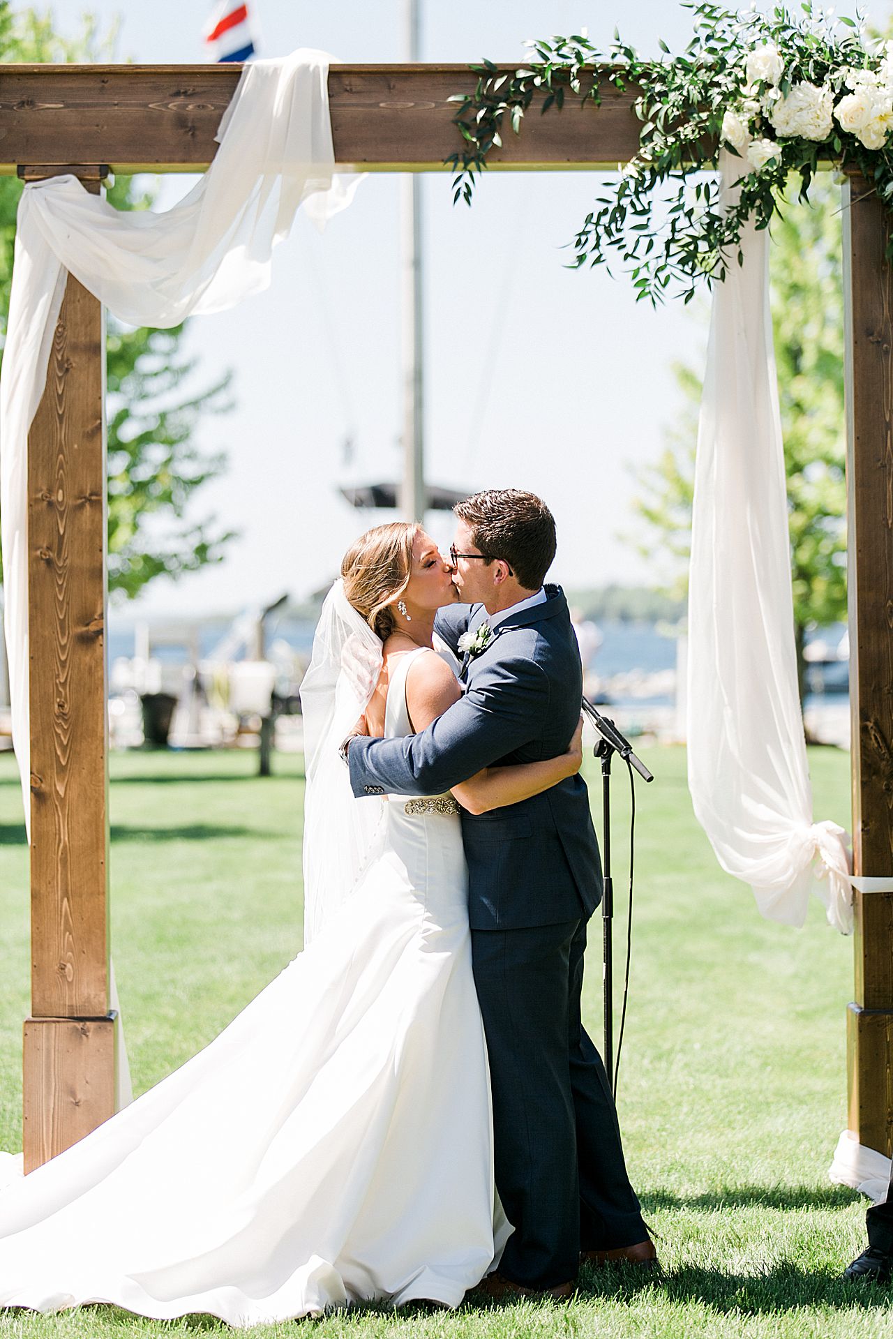 A Bride and Groom kissing under an arch with Lake Charlevoix in the background during their wedding ceremony