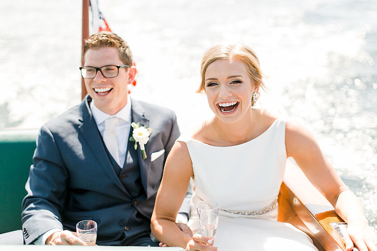 Bride and groom laughing while holding champagne during a boat ride on a sunny day in Northern Michigan