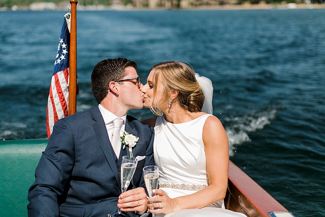 Bride and groom kissing while holding champagne on the back of a boat on Lake Charlevoix