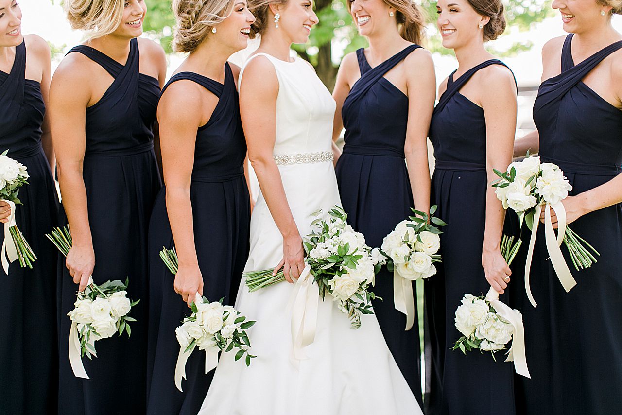 Bride and bridesmaids bouquets in their hands with white roses and white ribbon