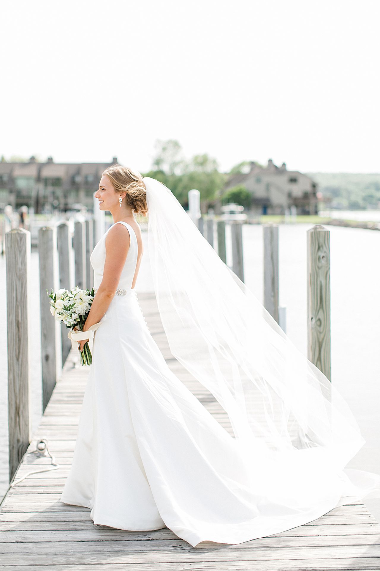Portrait of a bride looking to the left with her veil flowing into the wind on a dock in Northern Michigan
