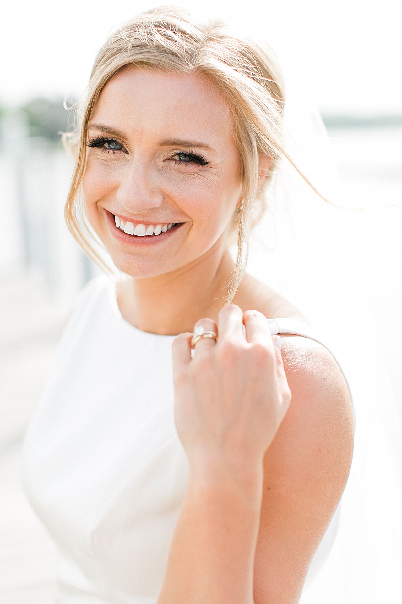 Portrait of a bride smiling at the camera with her left hand touching her shoulder