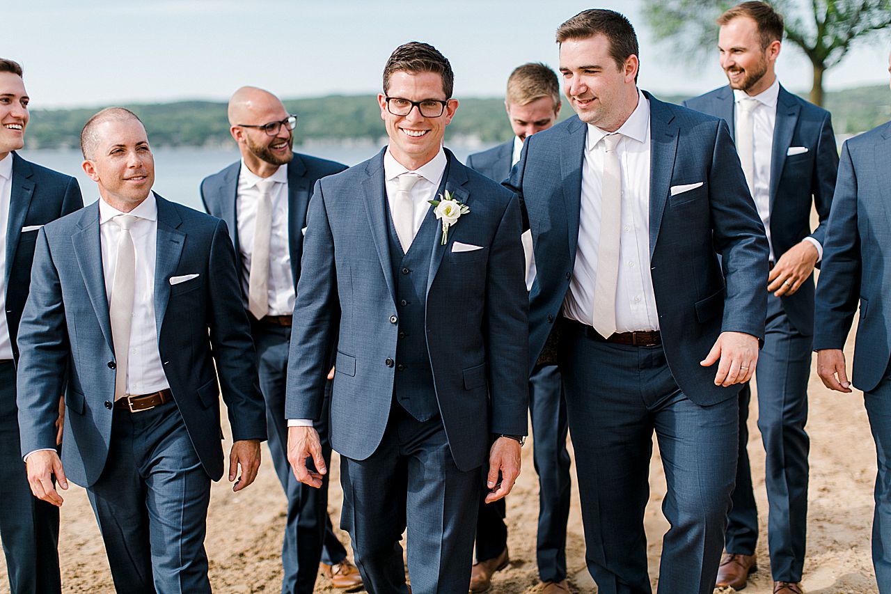 Groom and groomsmen walking and smiling at the beach in Boyne City, Michigan