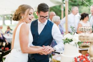 Bride and groom laughing while cutting into their white 2 tier wedding cake at the wedding reception at Boyne Mountain Resort on Deer Lake