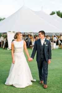 Bride and groom walking while holding hands outside of the reception tent on Deer Lake in Boyne Falls, Michigan