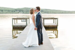 Bride and groom holding hands and kissing in the middle of a dock at dusk at Boyne Mountain Resort