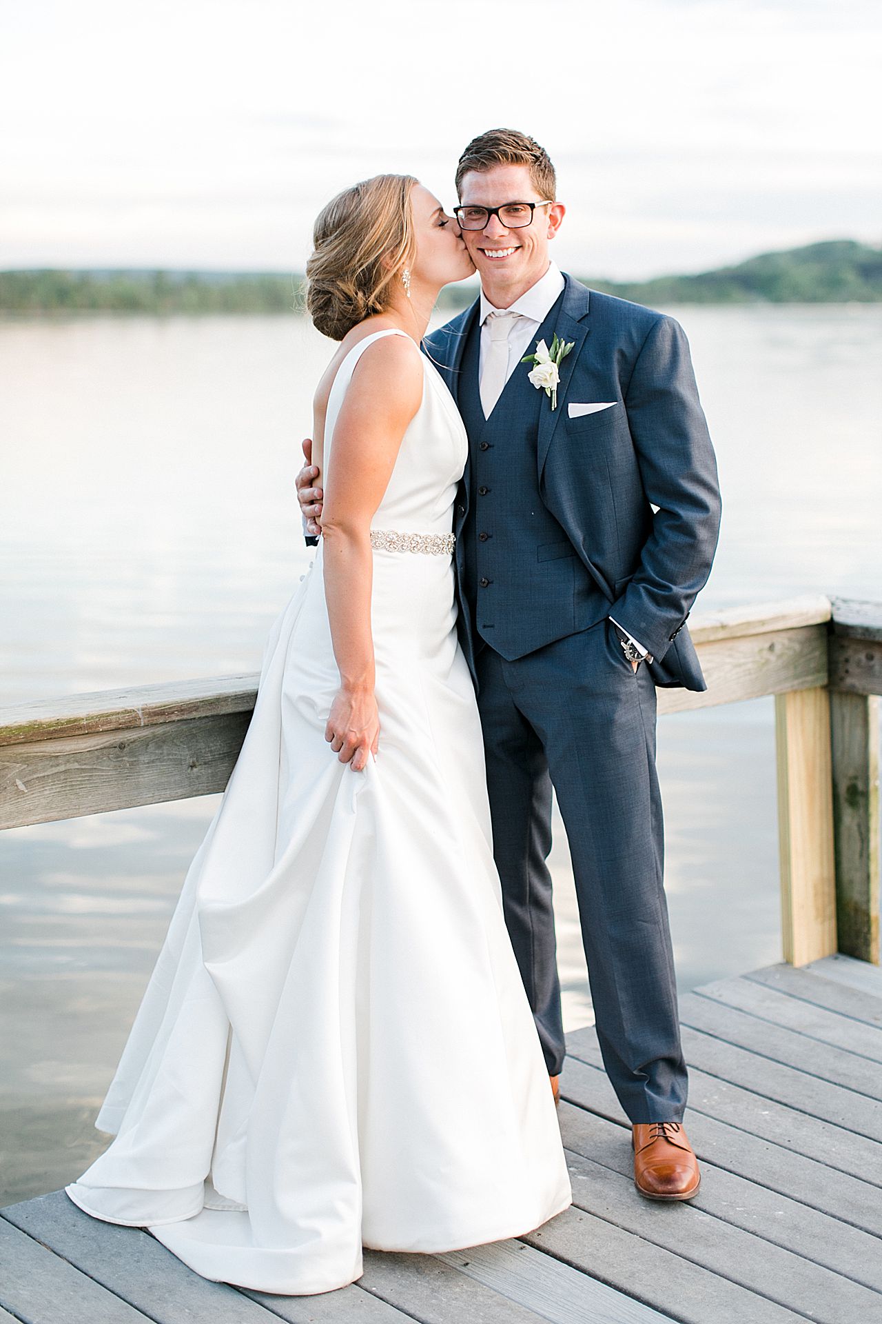 Bride kissing the grooms cheek while he smiles on Deer Lake in Boyne Falls, Michigan