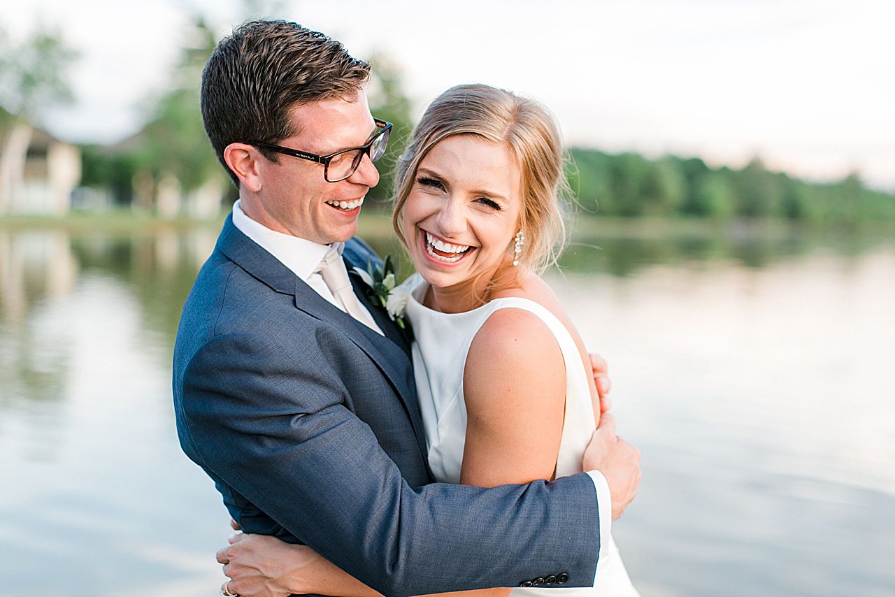 Bride laughing and smiling while the groom looks at her in Northern Michigan on Deer Lake at sunset